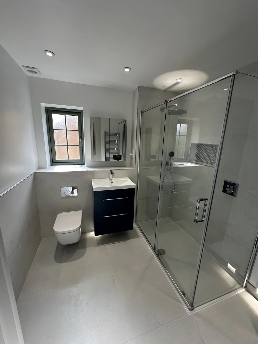 Fitted shower room with navy vanity, wall-hung WC and large glass shower enclosure — bathroom installation