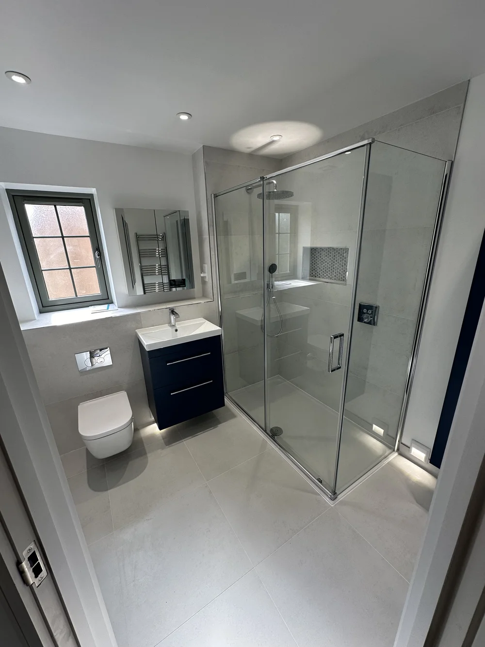 Fitted ensuite with navy vanity, wall-hung WC and corner shower enclosure — bathroom installation